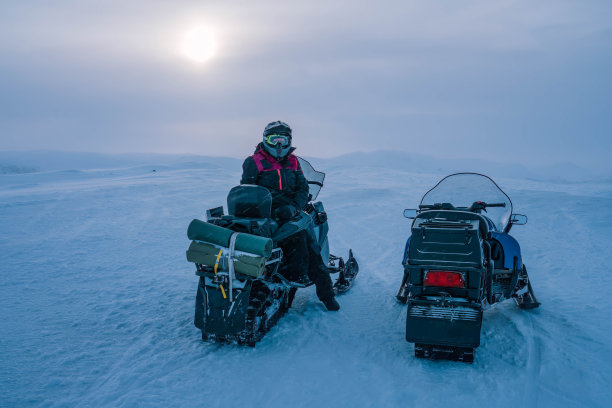两辆雪地车站在多雪多风的山顶，景色优美。一个人，整体，头盔坐在雪地摩托在照片的右侧，看着相机。瑞典拉普兰图片下载