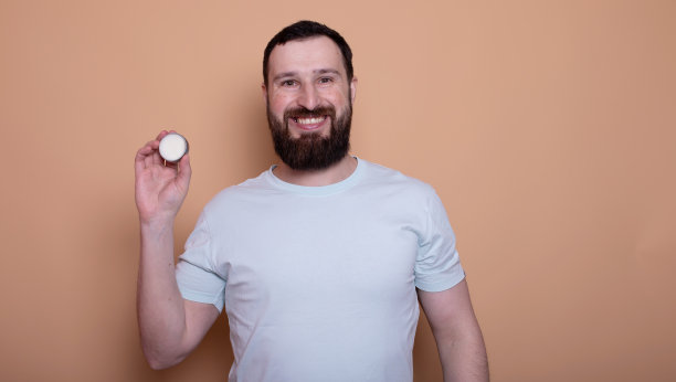 大胡子帅哥手持胡须膏的特写照片。图片下载