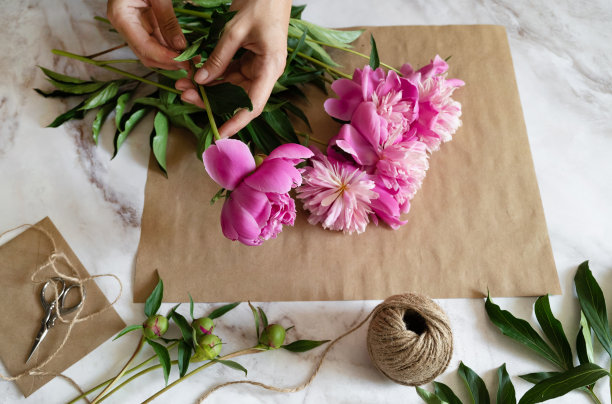 一位女花店老板在桌面上用牛皮纸包着一束牡丹花。从上面看。高质量照片图片下载