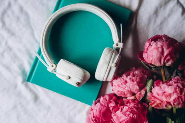 书，白色耳机和一束粉红色的牡丹在床上，俯视图。图片下载
