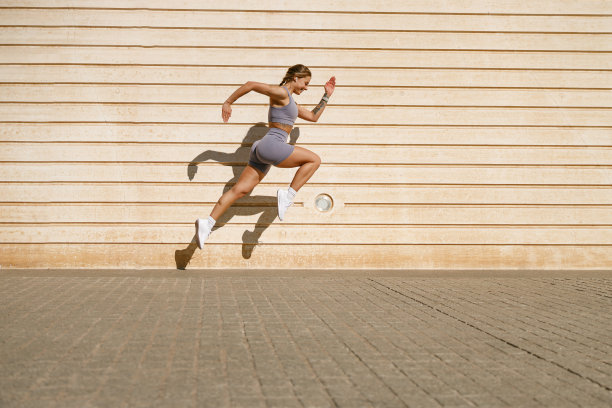 穿着运动服的年轻健康女子在户外的墙壁背景下在空中跳跃。高质量照片图片下载