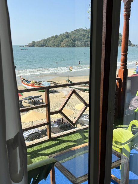 印度果阿，帕洛勒姆海滩，沙滩度假的图片，一排排成对的蓝色软垫太阳躺床，在沙滩上晒日光浴，停泊的渔船，从海滩小屋的滑动门，木栏杆上观看，重点是前景图片下载