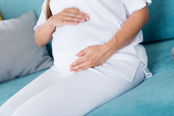 可爱温柔可爱的怀孕女孩未来的妈妈坐在沙发上抚摸腹部享受怀孕的照片图片下载
