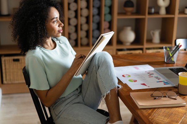 青年设计师工作项目。照片中的女人在现代阁楼里与新启动的项目一起工作。木桌上的通用设计笔记本图片下载