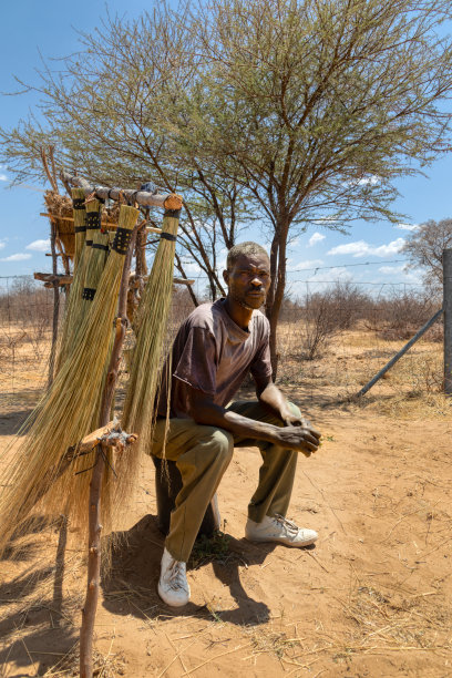 在一个阳光明媚的日子里，村里的街头小贩，一个非洲人站在高速公路边的扫帚架前图片下载