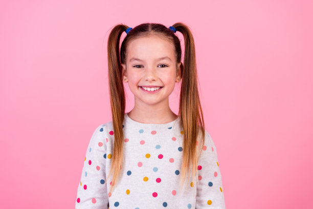 好心情的照片漂亮可爱的小女孩，尾巴发型，穿着时尚的圆点运动衫，微笑孤立在粉红色的背景图片下载