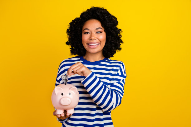 好心情的照片可爱的聪明的女人穿着条纹运动衫把钞票放在钱罐孤立的黄色背景图片下载