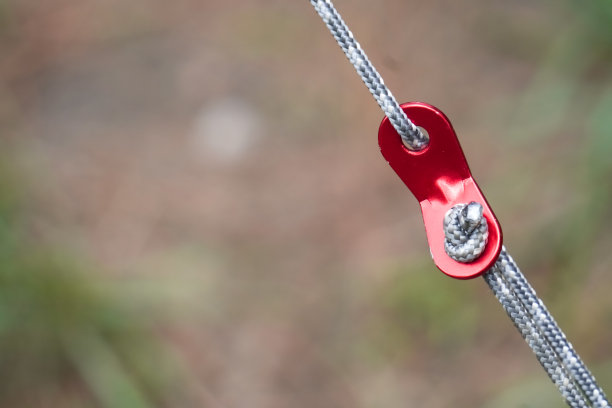 一个铝制工具的特写照片，上面有绳子，用来紧固和加强帐篷免受风和自然干扰。图片下载