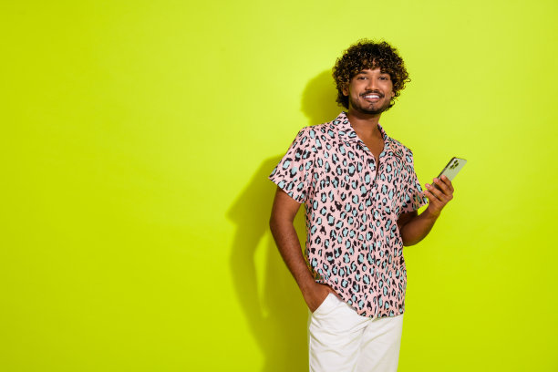 照片中英俊的年轻人手持电子产品购物，用户穿着流行的粉红色豹纹服装，孤立在黄色背景上图片下载