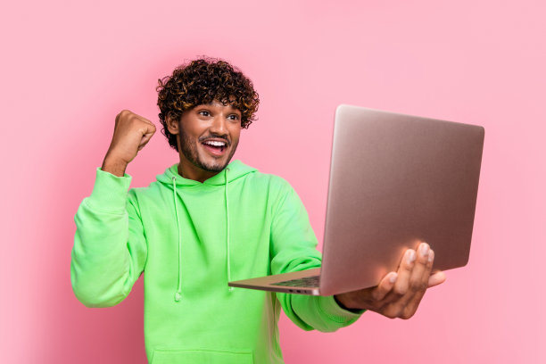 照片喜出于色的有趣的家伙沉迷于赌博游戏在线赌场持有笔记本电脑广告应用程序隔离在粉红色的背景图片下载