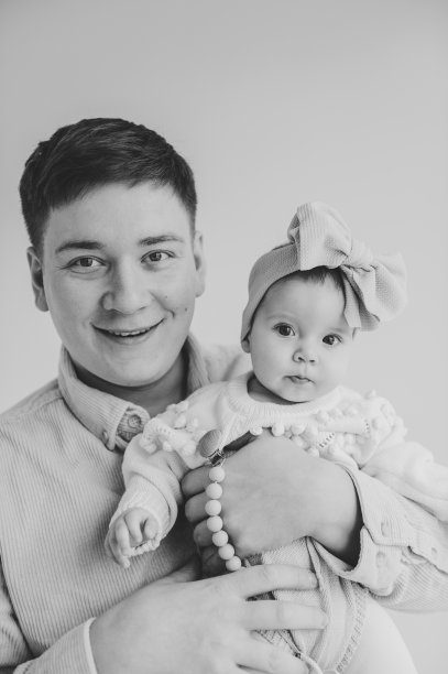 爸爸和小女孩的肖像，在墙的背景中被孤立。可爱的婴儿在爸爸的手臂特写。爸爸手里抱着6个月大的小女孩。父亲拥抱他的女儿。黑白照片图片下载