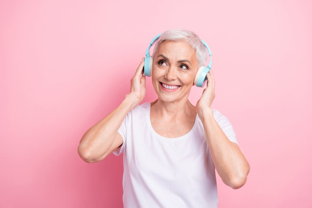 照片中可爱的老夫人的肖像触摸耳机，看起来空落落的穿着时尚的白色服装孤立在粉红色的背景图片下载