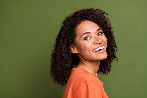 照片中闪亮梦幻的女士穿着橙色t恤微笑着回头看空旷孤立的卡其色背景图片下载