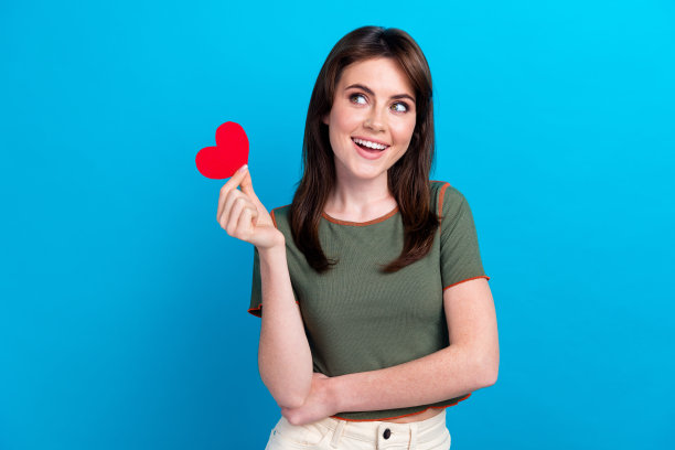 可爱的创意人物手持小心形符号卡片的照片，在蓝色背景上看起来空荡荡的图片下载
