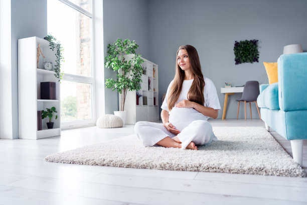 可爱可爱的妈妈欢快的怀孕的女孩坐在毛茸茸的地毯地板上抚摸肚子的照片图片下载