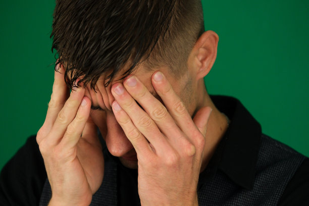 压力大的商人坐在他的办公桌前，双手抱着头的情绪，一个英俊的男人，一个绿色背景上的铬材质特写，深色头发的年轻人图片下载