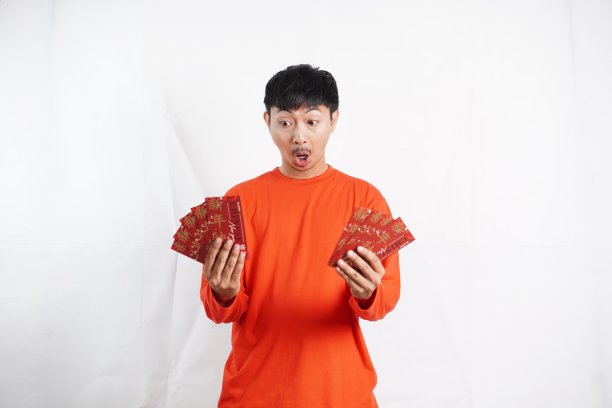 春节快乐。拿着红袍或红包的亚洲男子被隔离在白色背景上。祝你好运、问候和祝贺。有趣的脸图片下载