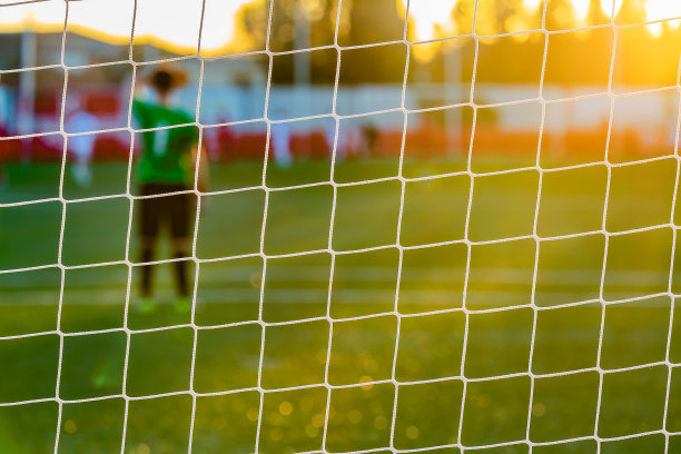 球门网的后视图，守门员遮挡额头的一部分，以保护自己免受刺眼的阳光图片下载