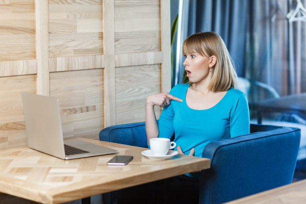 在笔记本电脑前工作的女人，用惊讶的表情指着自己。图片下载