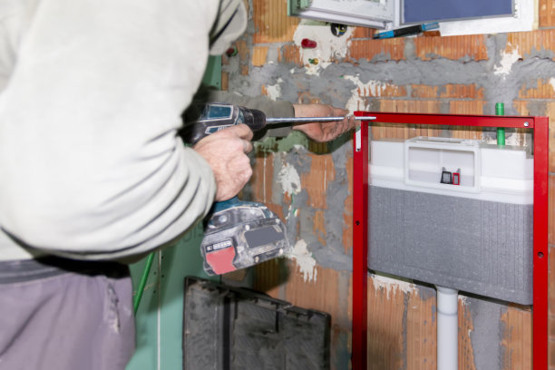 一名成熟有经验的水管工，在建筑工地用螺丝刀将壁挂式厕所的框架安装在砖墙上。图片下载