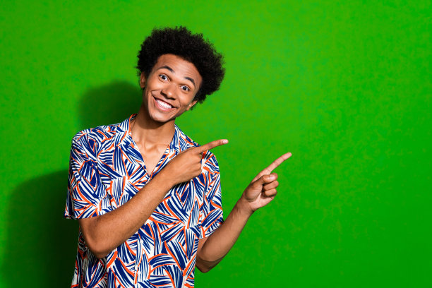 照片的家伙在印刷衬衫露齿微笑，并指出手指空白空间促销playstation 5游戏孤立的绿色背景图片下载