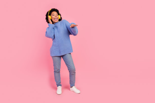 迷人的年轻女子的全身照片，耳机音乐dj派对穿着时尚的蓝色针织品衣服孤立在粉红色的背景图片下载
