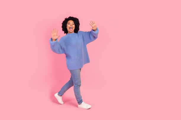 漂亮的年轻女孩走路挥手的全尺寸照片穿着时尚的蓝色针织服装孤立在粉红色的背景图片下载