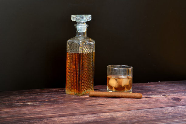 一个水晶醒酒器和一个多面威士忌玻璃杯，在木桌上放着冰块，旁边是一支古巴雪茄。图片下载