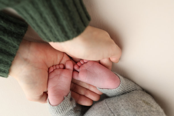 爸爸的手掌，妈妈都抱着刚出生的婴儿的脚。新生儿的脚放在父母的手掌上。工作室微距照片的孩子的脚趾，脚跟和脚在一个白色的背景。图片下载