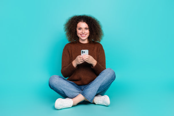 漂亮年轻女孩的全尺寸照片坐在地板上拿着电话电子商务穿着时髦的棕色衣服孤立在青色背景图片下载