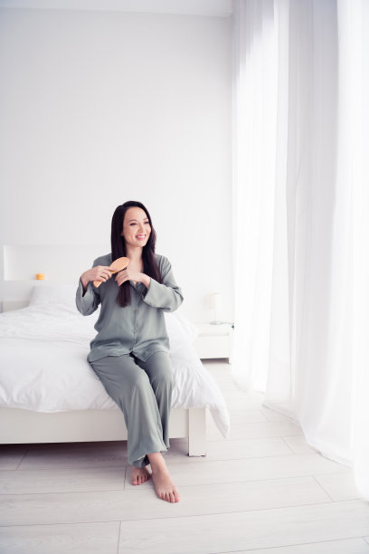 照片肖像漂亮的年轻女孩坐梳头发日常穿着时尚的灰色睡衣孤立在舒适的现代白色卧室图片下载