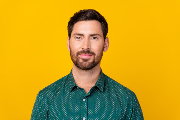 照片中，一个积极、开朗、满意的深色头发的男人，穿着带点的衬衫，在充满活力的黄色背景下微笑着图片下载
