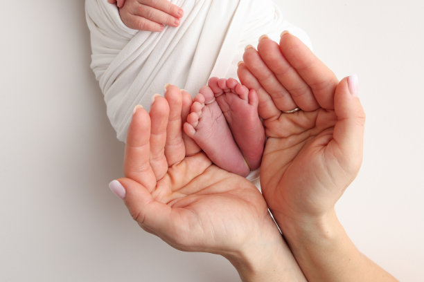 爸爸的手心，妈妈的脚上都抱着刚出生的婴儿的白毯子。新生儿的脚放在父母的手掌上。工作室微距照片的一个孩子的脚趾，脚跟和脚。图片下载