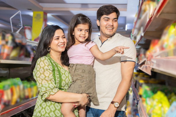 幸福的印度一家三口在超市买杂货。小女孩指着产品。图片下载