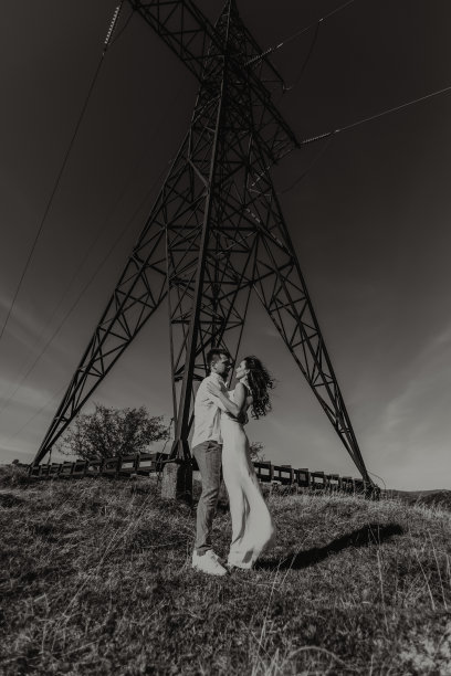 时尚的模特夫妇在夏天的山上。一个小男孩和一个穿着白色丝绸连衣裙的小女孩站在大型电线附近。黑白对比照片图片下载