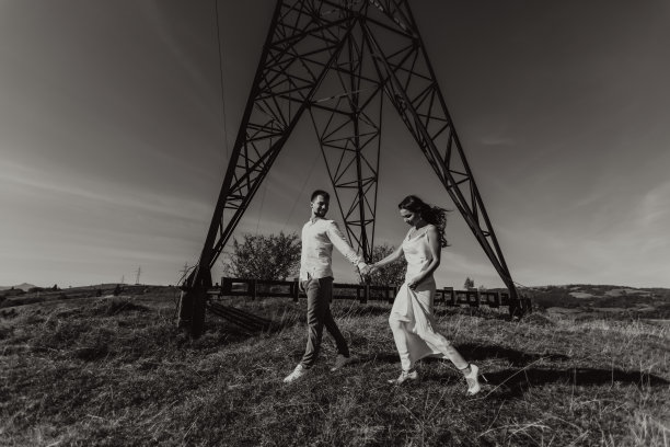 时尚的模特夫妇在夏天的山上。一个小男孩和一个穿着白色丝绸连衣裙的小女孩站在大型电线附近。黑白对比照片图片下载