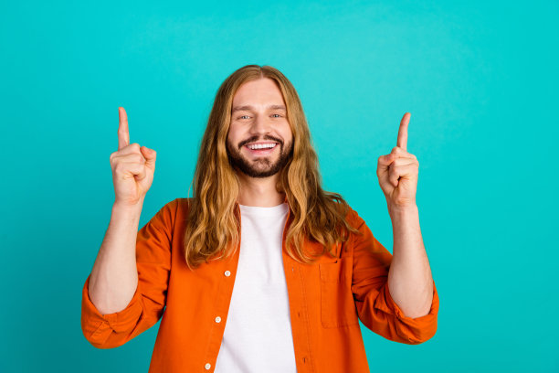 照片中，穿着橙色衬衫的微笑年轻人手指指向上方，在青色背景下为和平社区举办嬉皮士派对图片下载