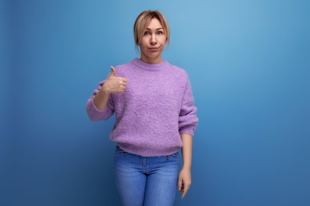 愉快的金发碧眼的年轻女子在紫色的毛衣显示喜欢与手在蓝色背景与复制空间图片下载
