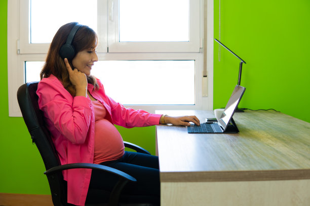 孕妇带着笔记本电脑和耳机在办公室工作的照片。本空间图片下载