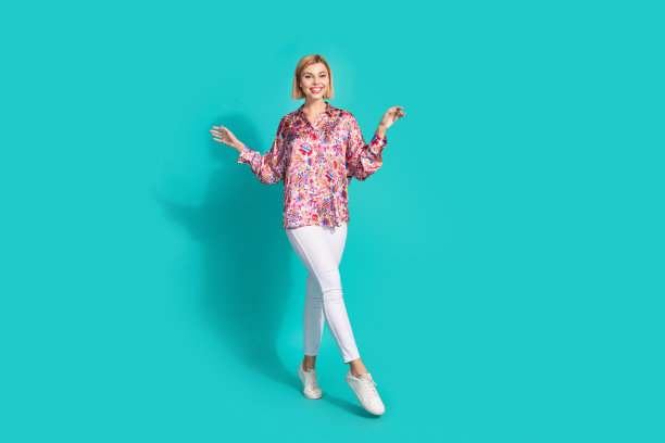 全尺寸照片可爱优雅的女孩穿着超大衬衫白色裤子显示运动鞋在脚上孤立的绿松石色背景图片下载