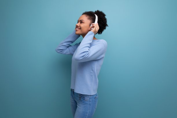 时尚的照片肖像，精力充沛的20多岁的年轻黑人黑发女子听音乐，使用白色无线耳机的工作室背景与复制空间图片下载