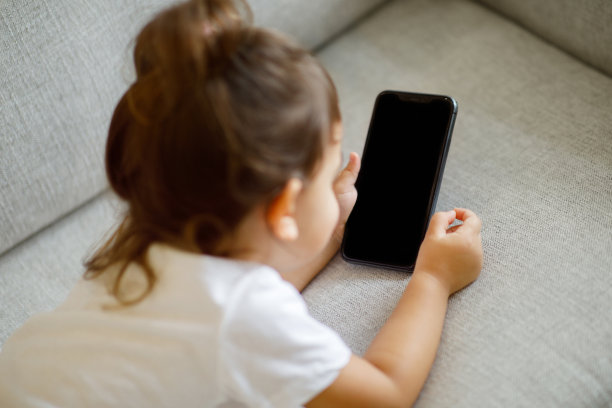 小女孩躺在舒适的沙发上，使用空白屏幕的智能手机图片下载