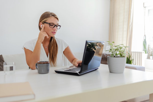 一名年轻女子在家工作时用笔记本电脑打视频电话的照片。女商人在家工作时在视频会议上微笑的照片。图片下载
