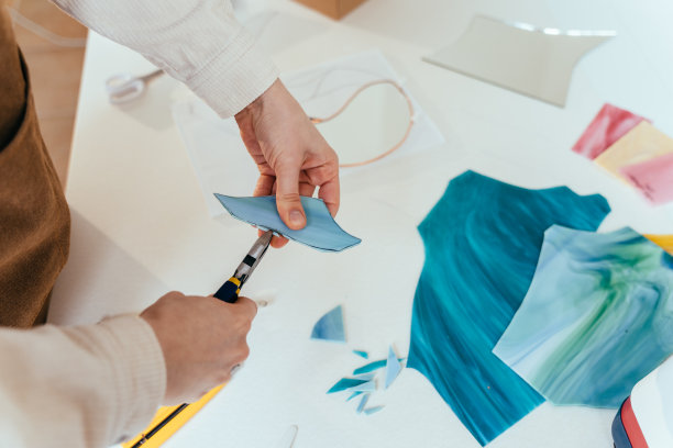 彩色玻璃工作流程中的不同步骤。在彩色玻璃窗的艺术工作室里，专注的女人拿着一块玻璃进行创作。图片下载