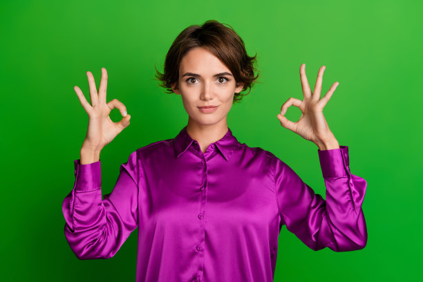 照片中，自信迷人的女士穿着时尚的品红色衣服，对产品质量满意，标志孤立在绿色背景上图片下载