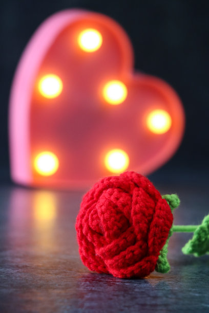 钩针玫瑰的特写图片，红色的花瓣，绿色的茎和叶，粉红色的心形盒子内衬安装照明，灯泡，黑色背景，情人节和浪漫的概念图片下载