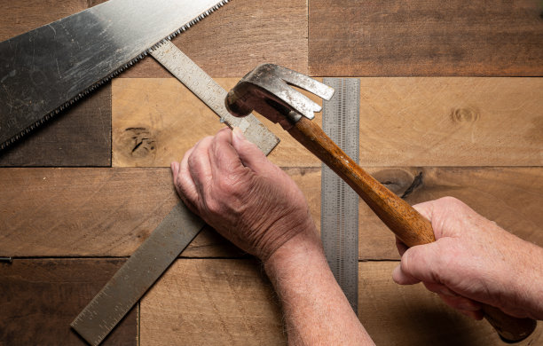 照片中，男子用手在粗糙的木头背景上用手工具钉钉子图片下载