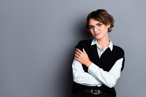 照片中梦幻迷人的女投资人戴着黑色马甲眼镜抱着自己空旷的空间孤立灰色背景图片下载