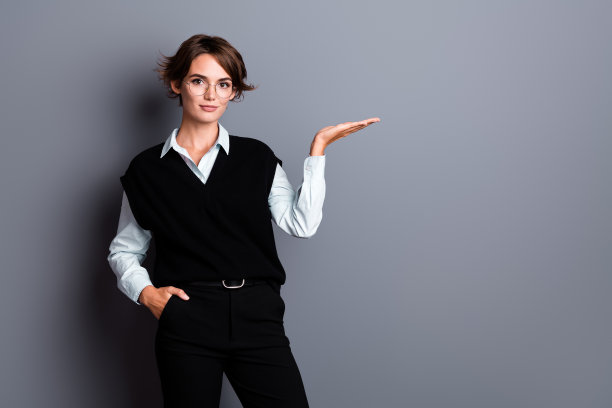 照片中漂亮甜美的女房地产经纪人戴着黑色马甲眼镜，手抱着空白空间孤立的灰色背景图片下载