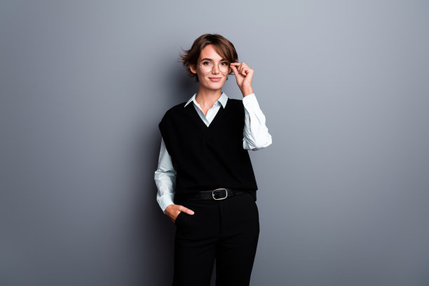 照片中聪明伶俐的女老师身穿黑色马甲，手挽眼镜，背景为孤立的灰色图片下载